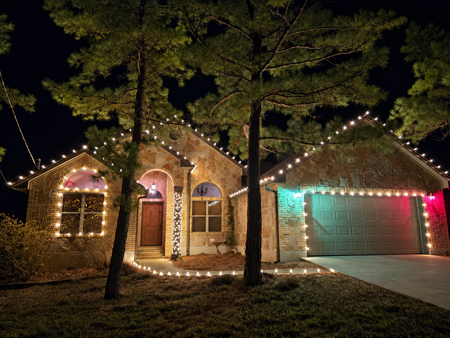 Stone-and-brick Bastrop home with trees, roofline, and pathway lights